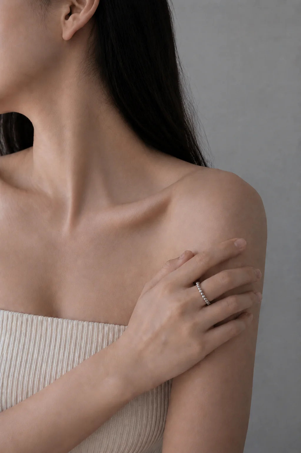 Close-up of a person wearing a delicate ring on a neutral background