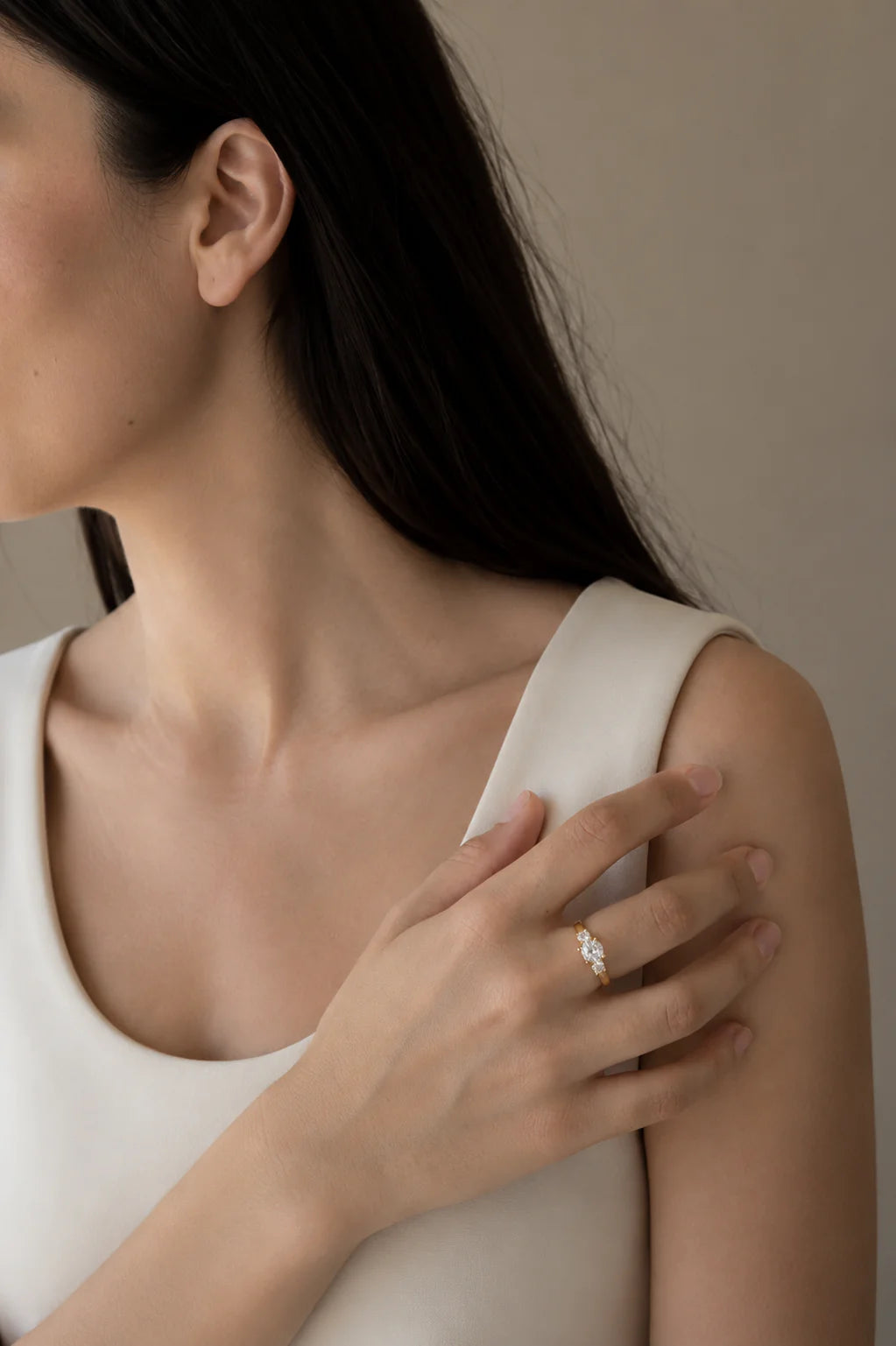 Woman wearing a white sleeveless top with a neutral background with 3 stone diamond ring