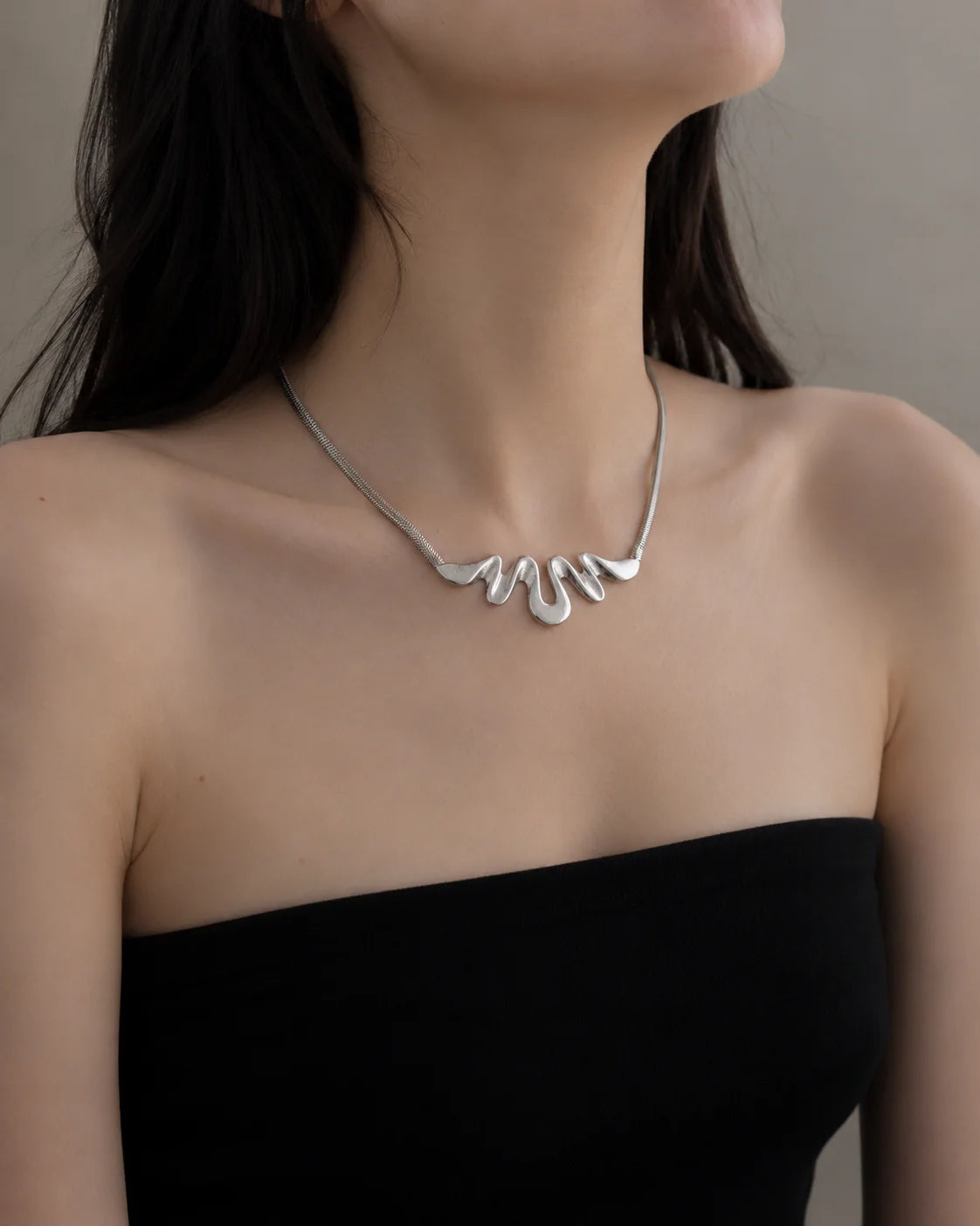 Silver necklace worn by a person against a neutral background