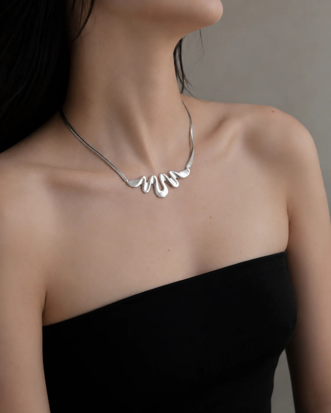 Silver necklace worn by a model against a neutral background