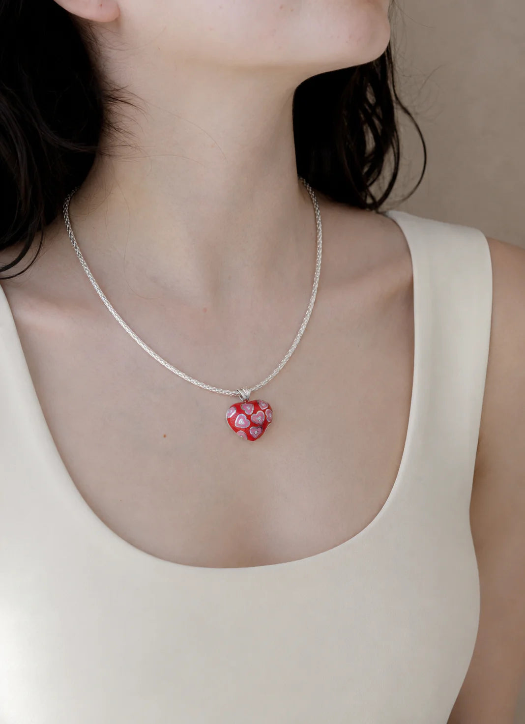 Necklace with a red floral pendant worn by a person in a beige top.