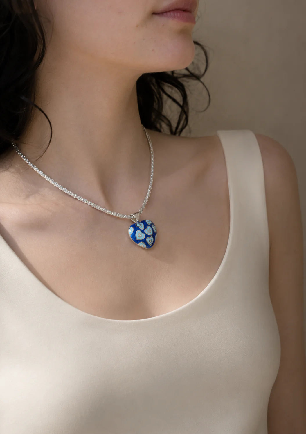 Necklace with a blue heart pendant worn by a person in a beige top.