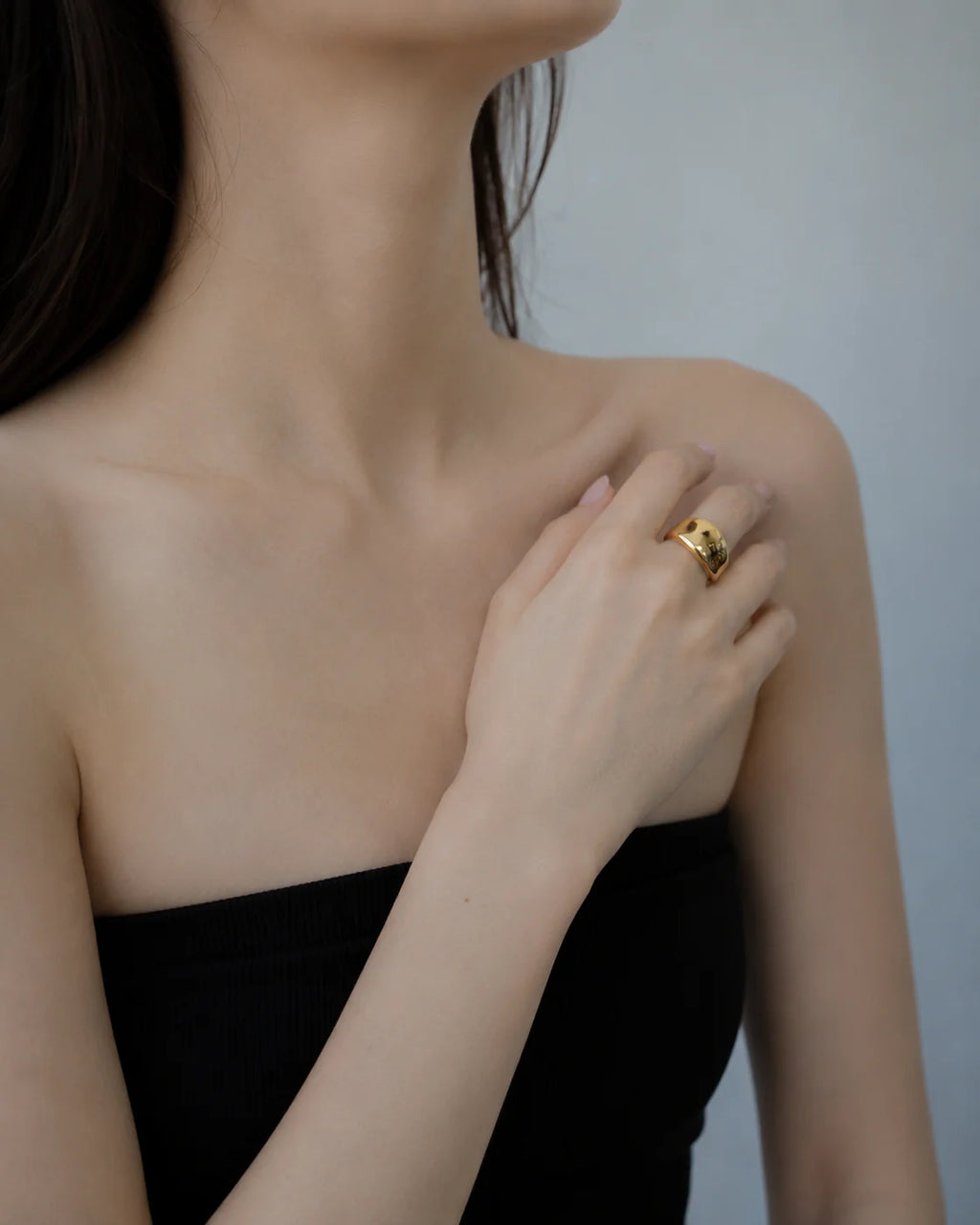 Woman wearing a gold ring on her hand against a neutral background