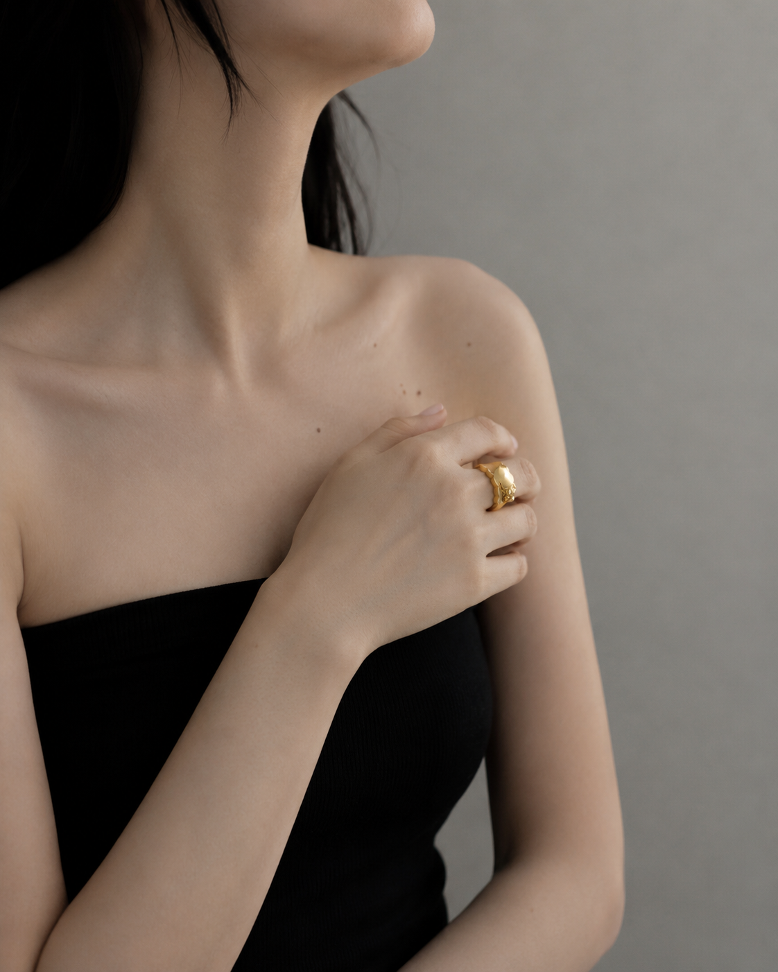 Woman wearing a gold ring on her hand against a neutral background
