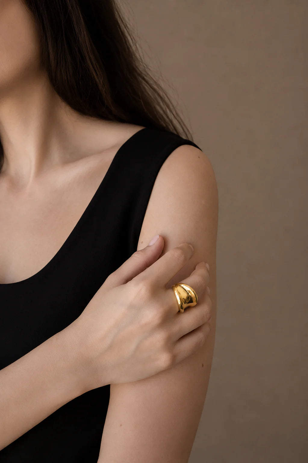 Woman wearing a gold ring on her hand against a brown background