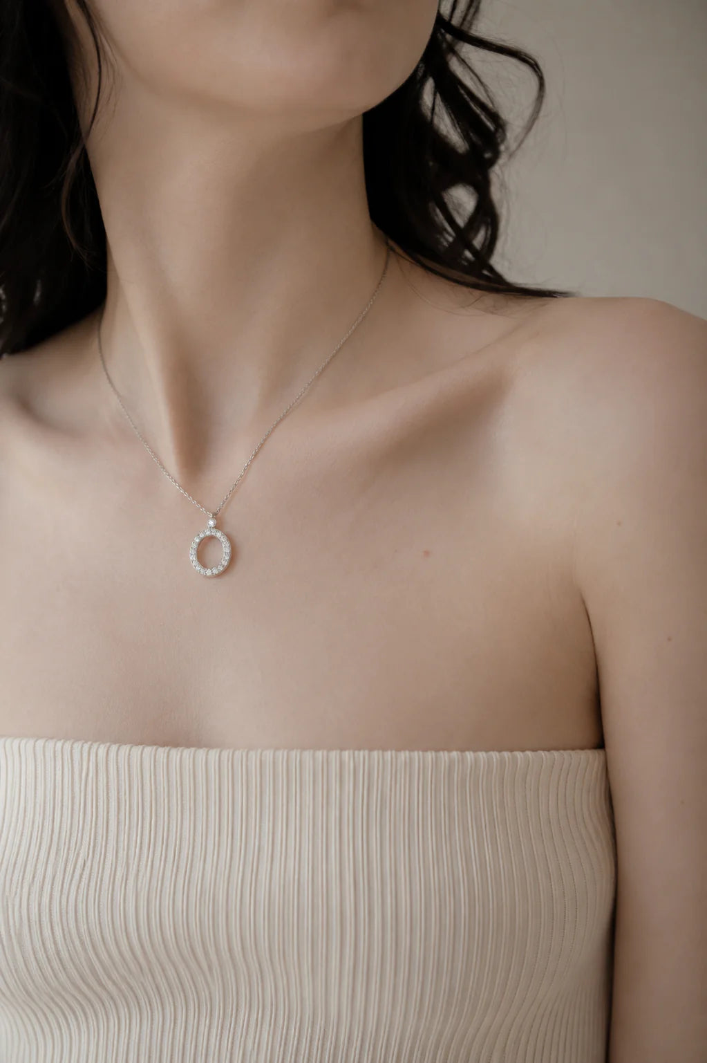 Necklace with a circular pendant worn by a person in a beige top against a neutral background