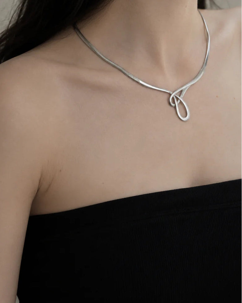 Silver necklace worn by a person against a neutral background