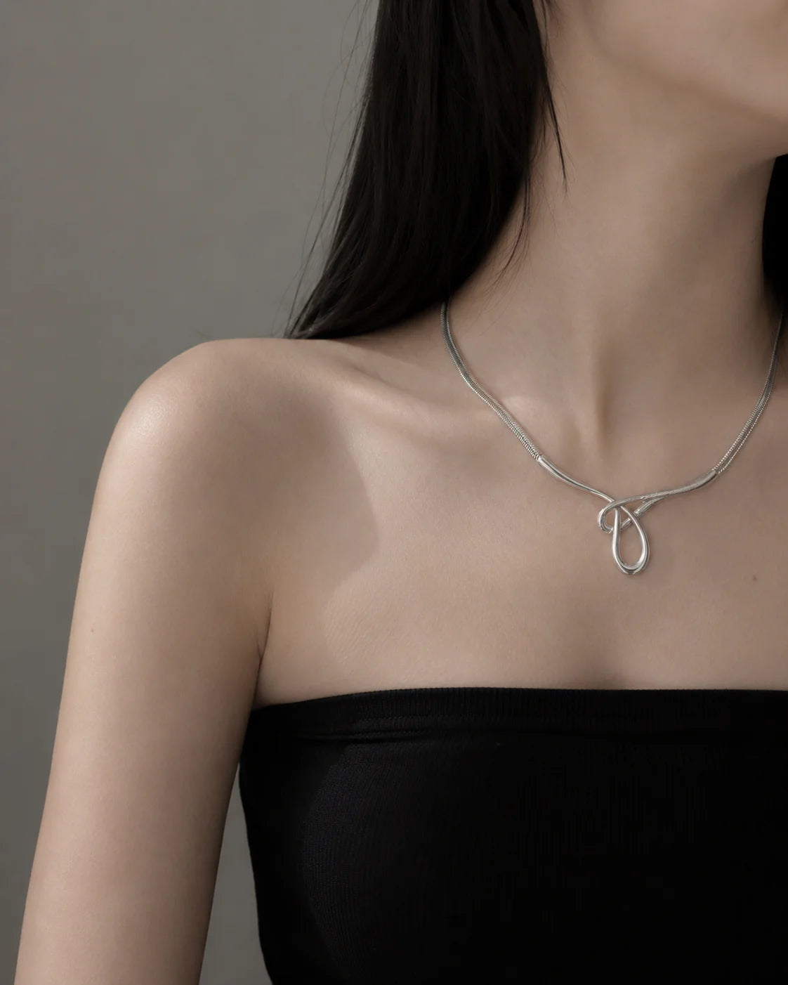 Silver necklace with a unique design worn by a person against a neutral background