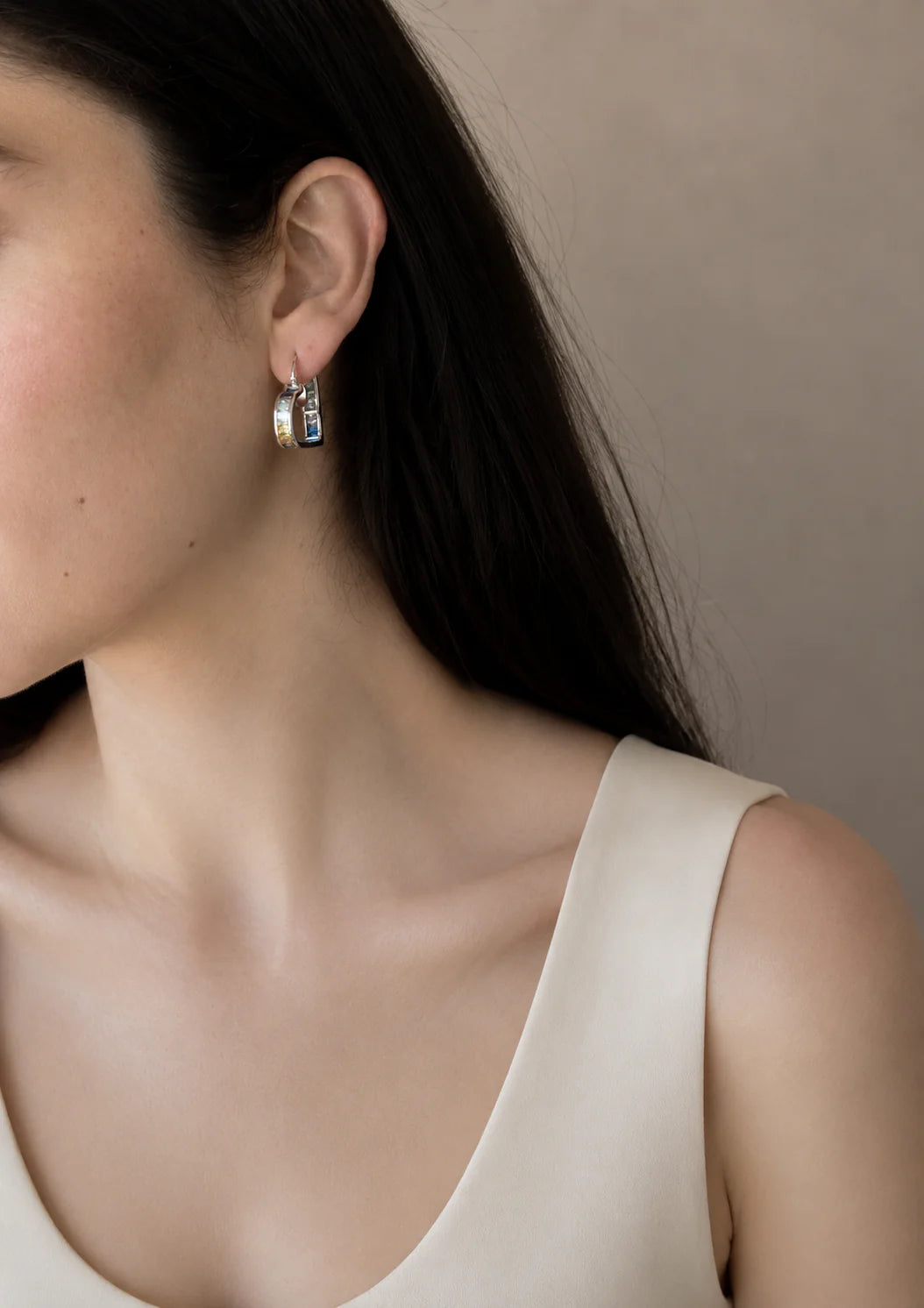 Close-up of a person wearing silver hoop earrings with a neutral background