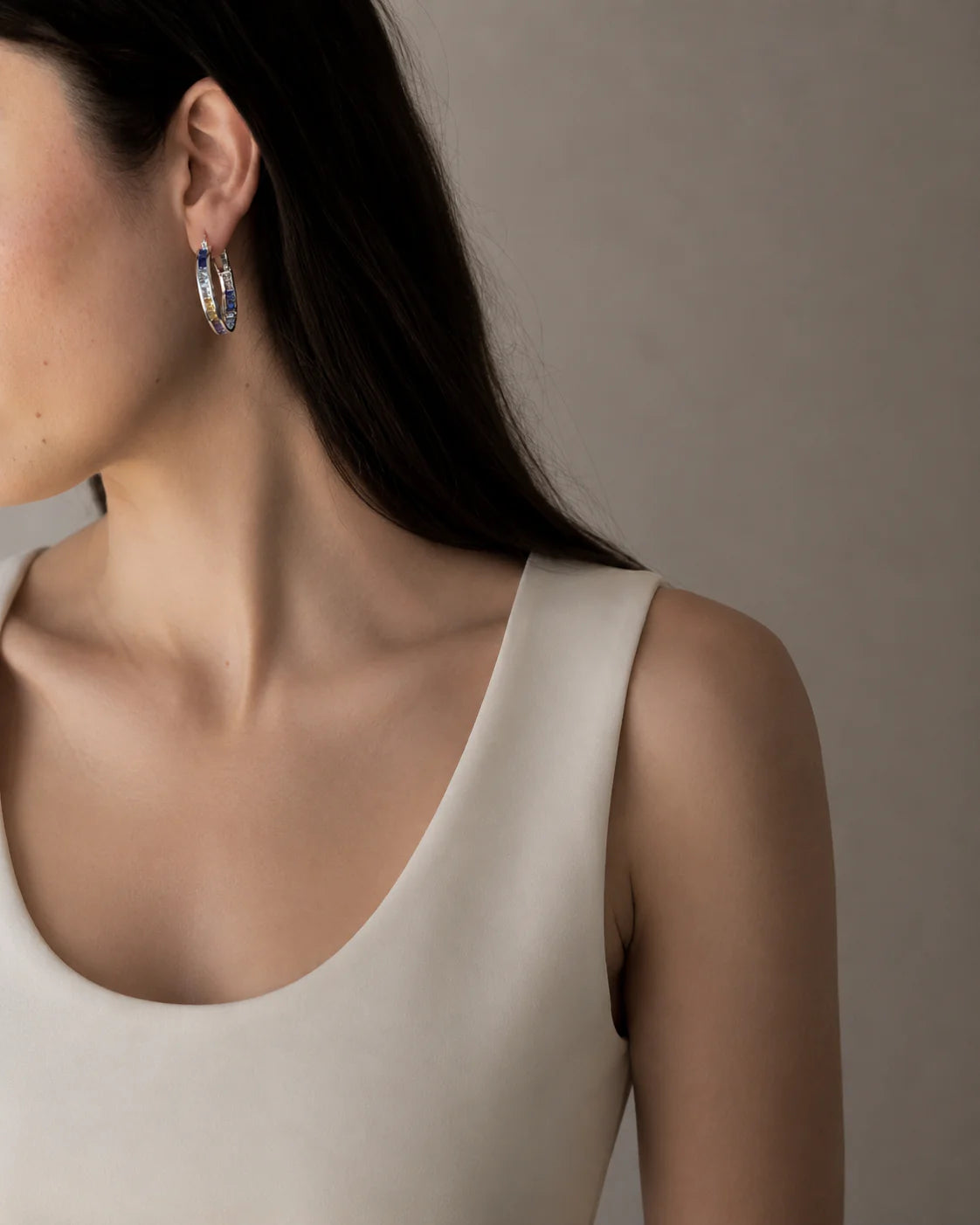 Close-up of a person wearing hoop earrings with a neutral background