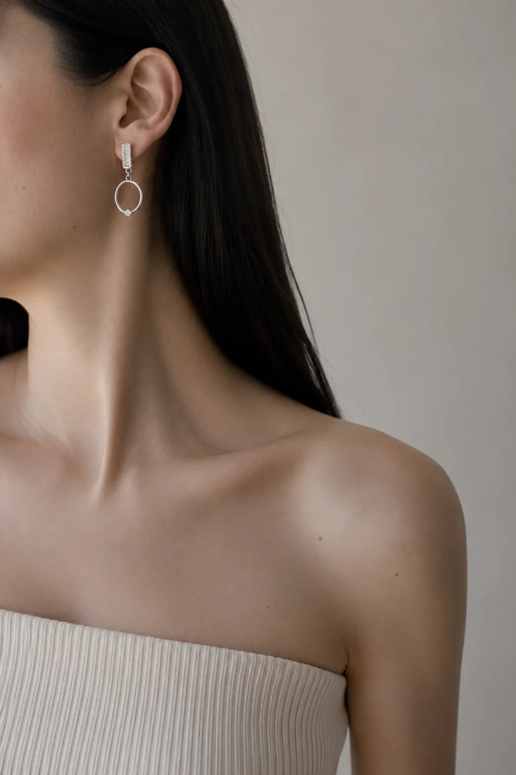 Close-up of a person wearing a silver hoop earring against a neutral background