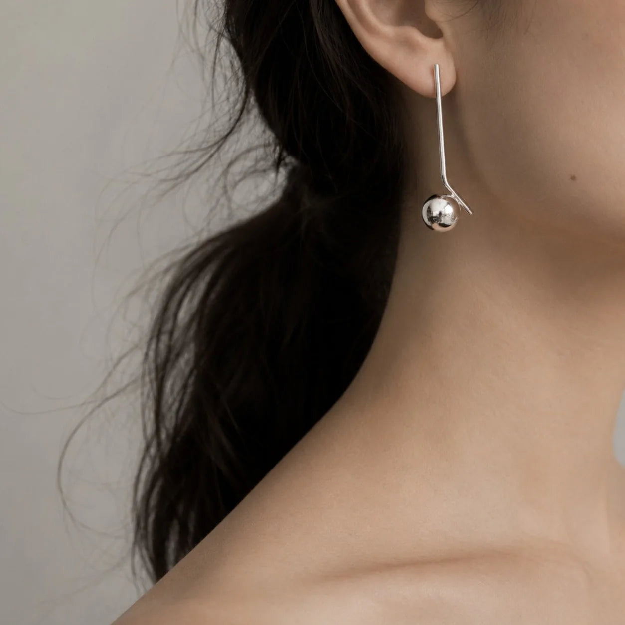 Silver earring worn by a person with a neutral background