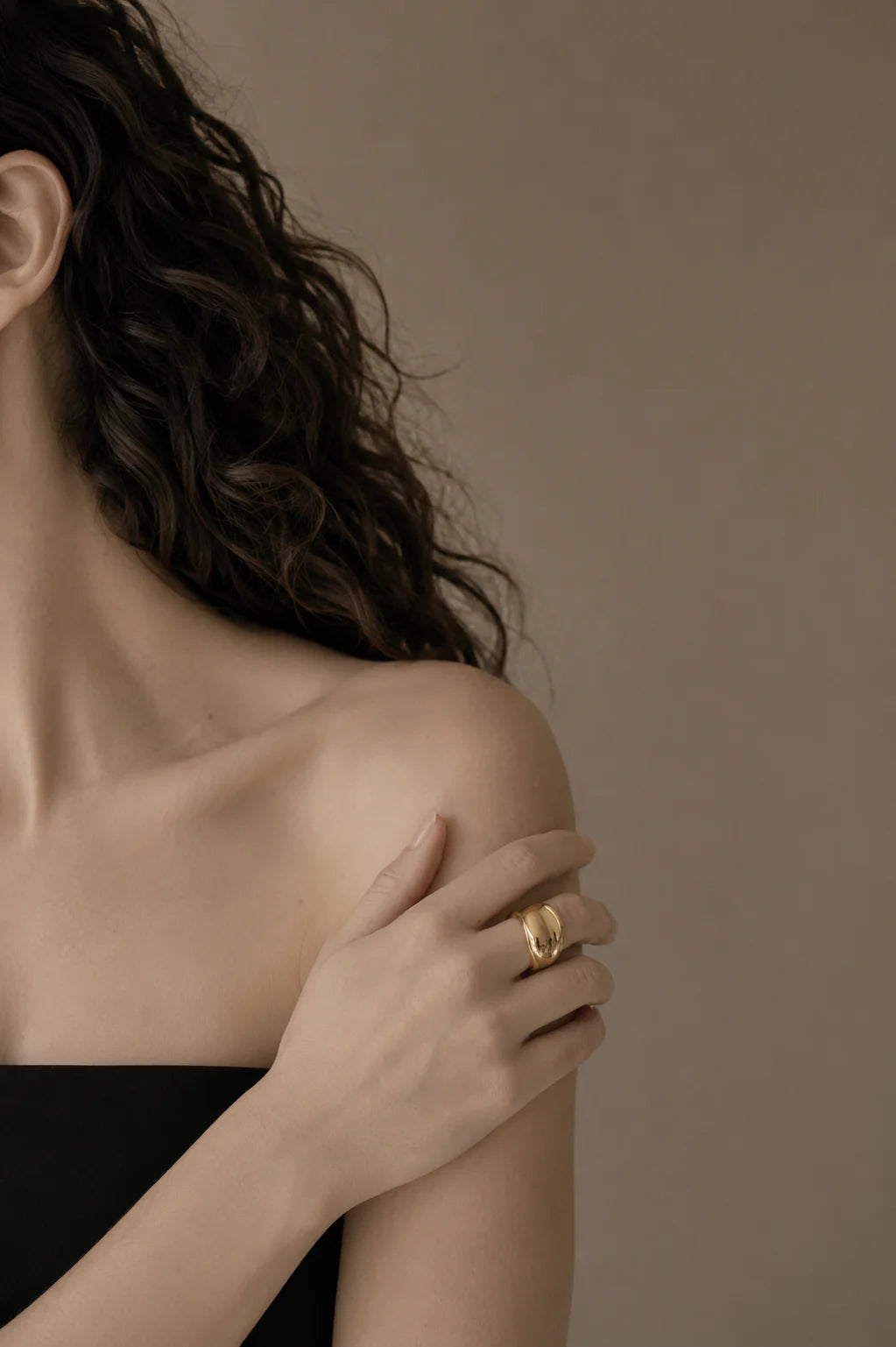Woman wearing a gold ring on her hand against a neutral background