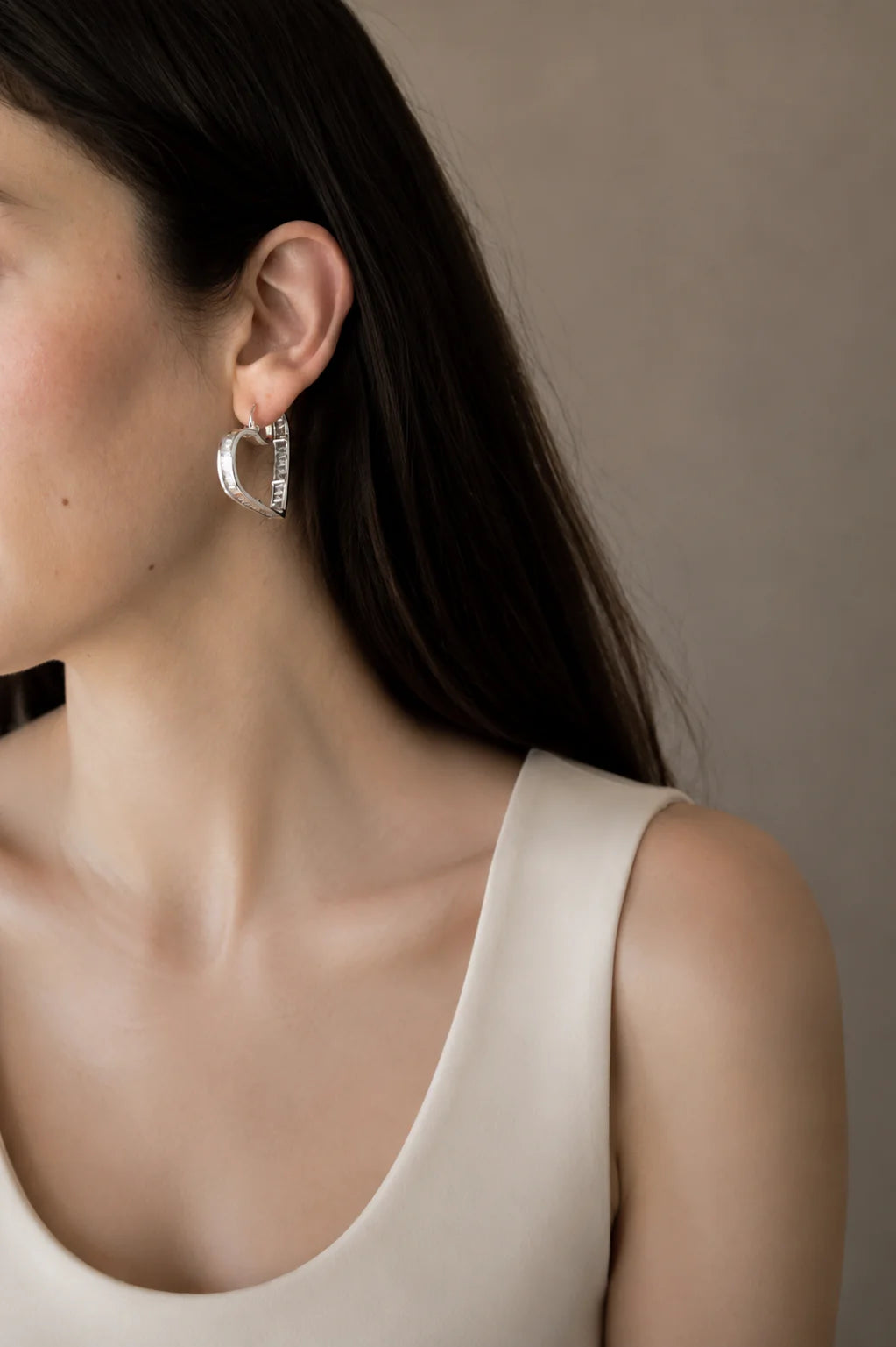 Close-up of a person wearing silver hoop earrings with a neutral background