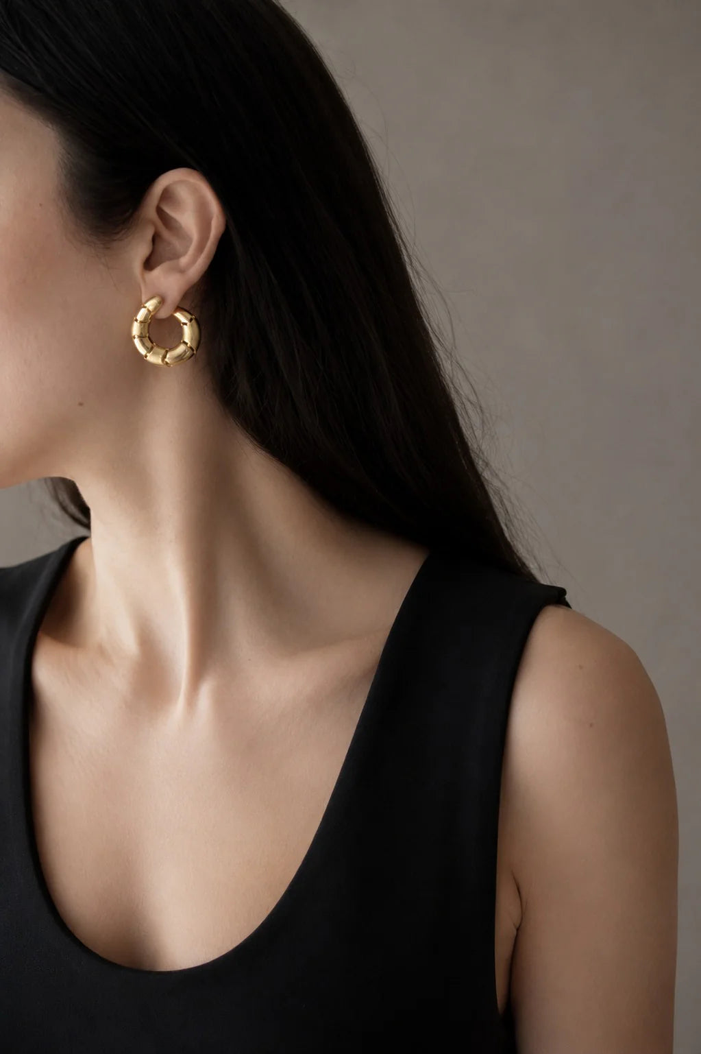 Gold hoop earrings worn by a person with a neutral background