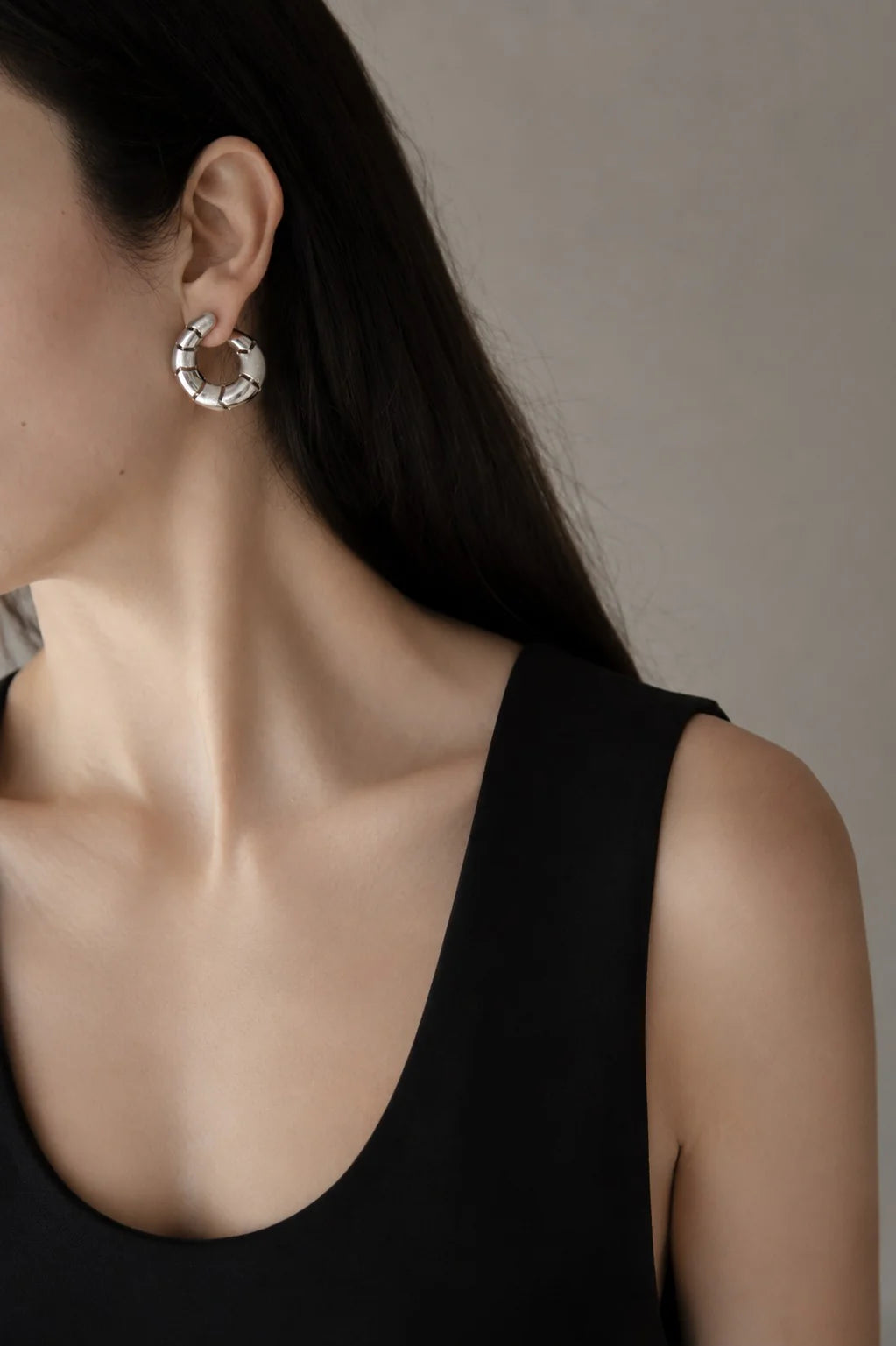 Close-up of a person wearing a silver hoop earring against a neutral background