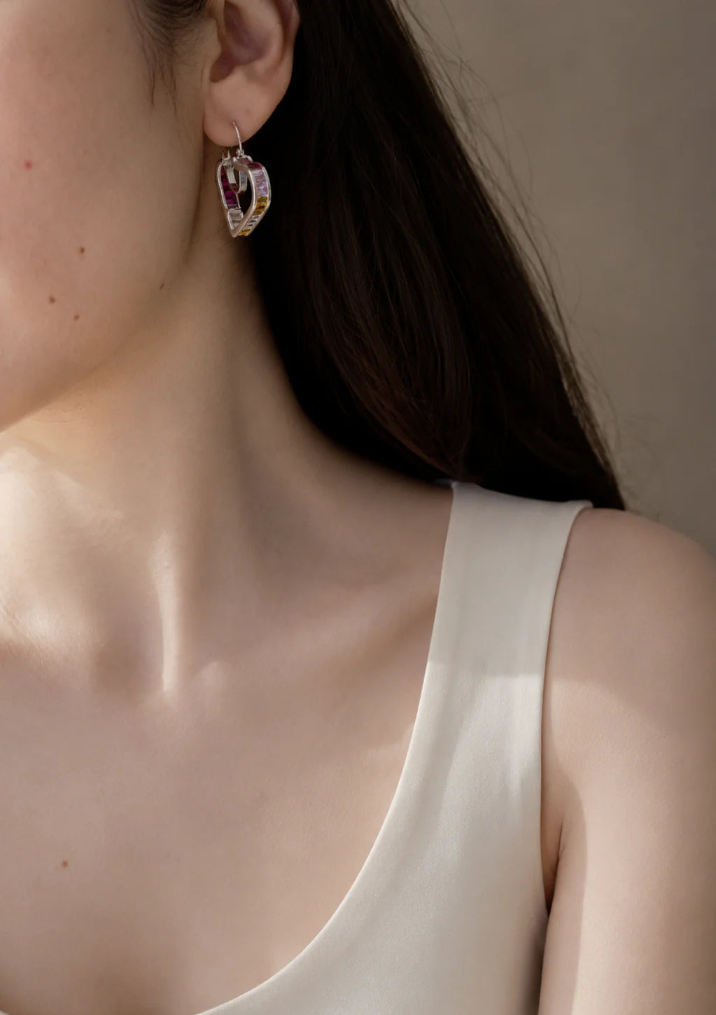 Close-up of a person wearing a heart-shaped earring with a neutral background