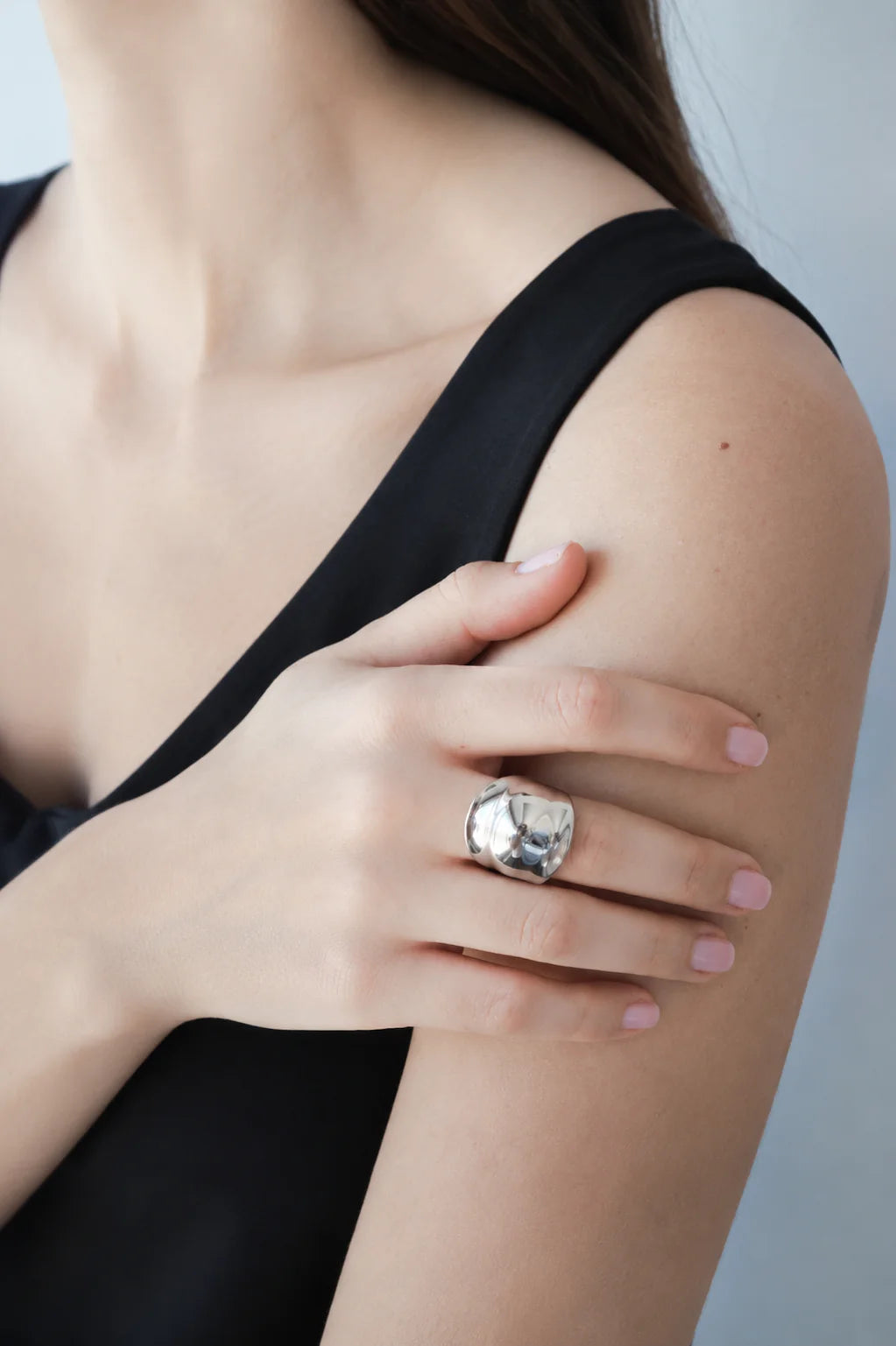 Person wearing a large silver ring on their hand against a neutral background