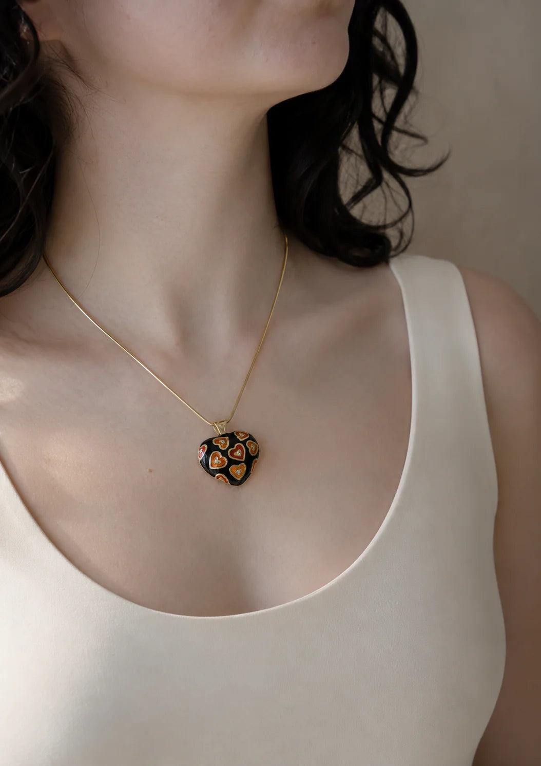 Hearth shaped Necklace with a decorative pendant worn by a person in a plain background