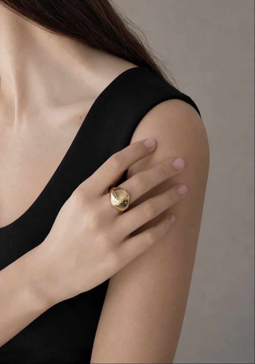 Close-up of a person wearing a gold ring on a neutral background