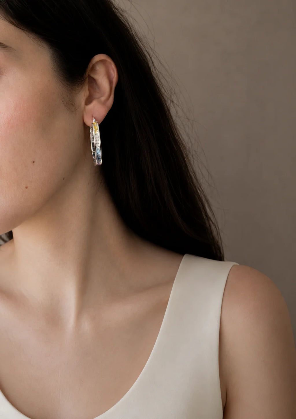 Close-up of a person wearing hoop earrings with a neutral background