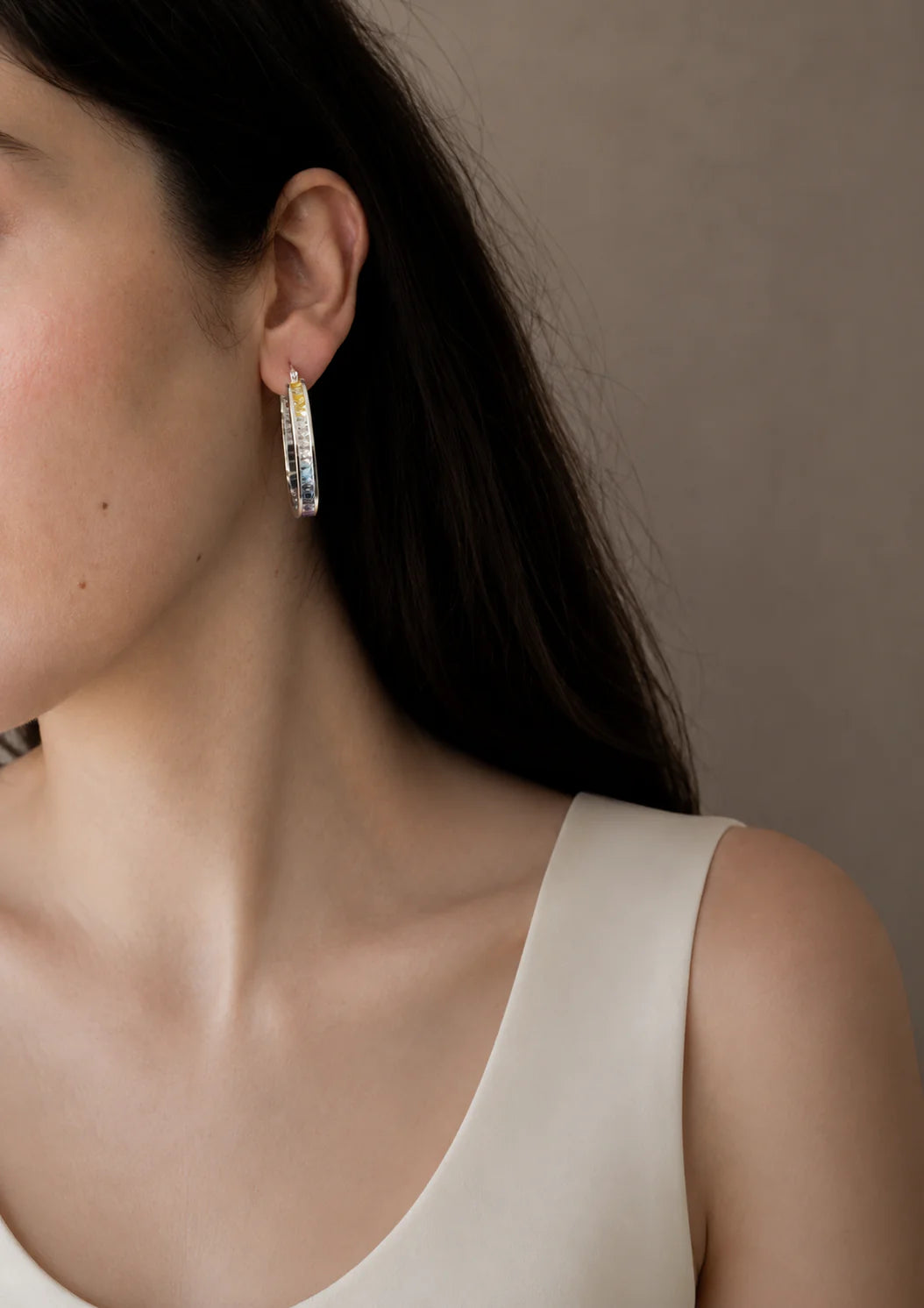 Close-up of a person wearing hoop earrings with a neutral background