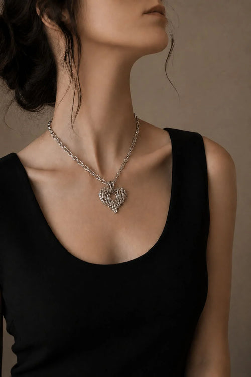 Person wearing a silver heart-shaped necklace against a neutral background