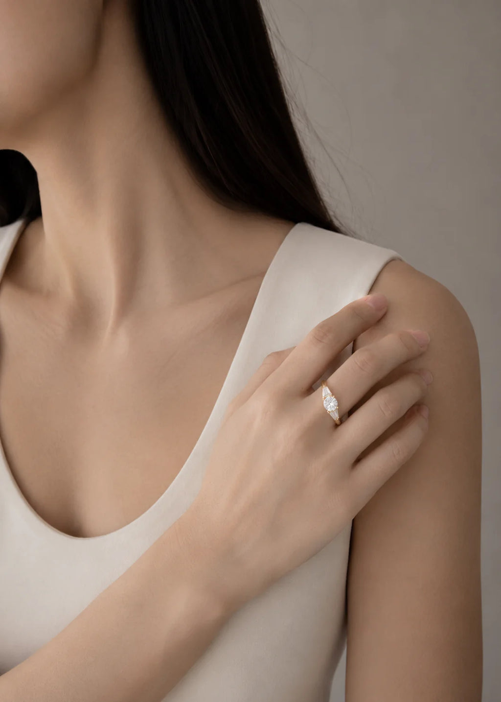 Close-up of a person wearing a diamond ring on a neutral background