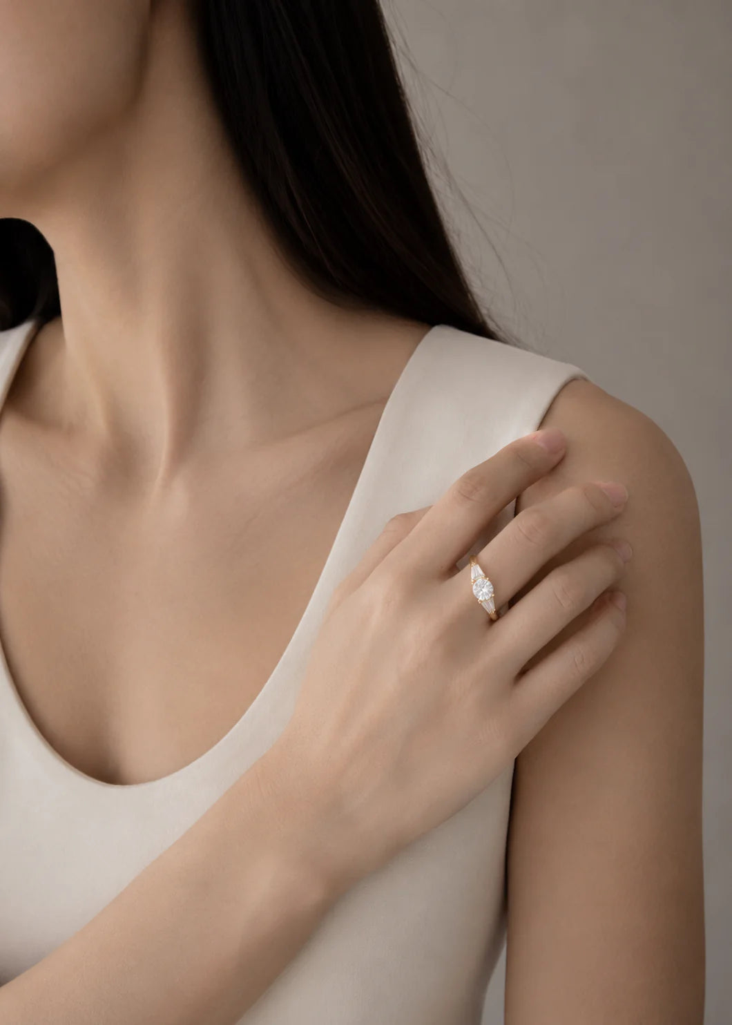 Close-up of a person wearing a diamond ring on a neutral background