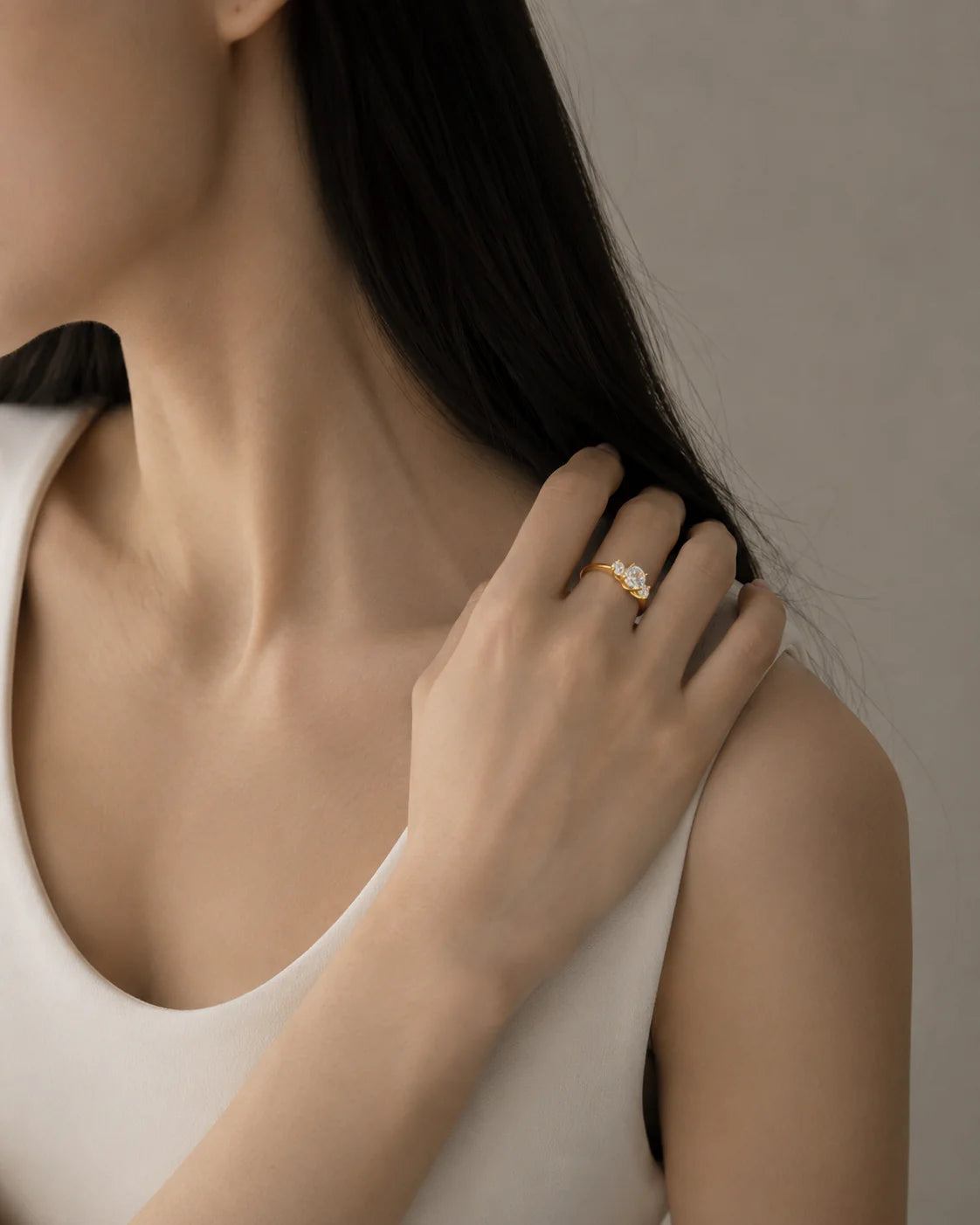 Close-up of a person wearing a gold ring with a diamond on a neutral background